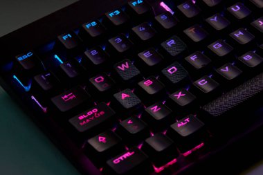 Renkli bir RGB mekanik oyun klavyesinin yakın çekimi canlı renklerle aydınlatılmış. Oyun ayarları için tasarlanmış modern bilgisayar aksesuarı, kişiselleştirilebilir arka ışıklandırma ve şık tasarım. 