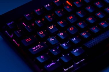 Renkli bir RGB mekanik oyun klavyesinin yakın çekimi canlı renklerle aydınlatılmış. Oyun ayarları için tasarlanmış modern bilgisayar aksesuarı, kişiselleştirilebilir arka ışıklandırma ve şık tasarım. 