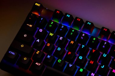 Renkli bir RGB mekanik oyun klavyesinin yakın çekimi canlı renklerle aydınlatılmış. Oyun ayarları için tasarlanmış modern bilgisayar aksesuarı, kişiselleştirilebilir arka ışıklandırma ve şık tasarım. 