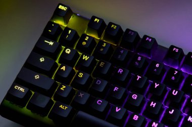 Renkli bir RGB mekanik oyun klavyesinin yakın çekimi canlı renklerle aydınlatılmış. Oyun ayarları için tasarlanmış modern bilgisayar aksesuarı, kişiselleştirilebilir arka ışıklandırma ve şık tasarım. 