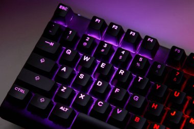 Renkli bir RGB mekanik oyun klavyesinin yakın çekimi canlı renklerle aydınlatılmış. Oyun ayarları için tasarlanmış modern bilgisayar aksesuarı, kişiselleştirilebilir arka ışıklandırma ve şık tasarım. 