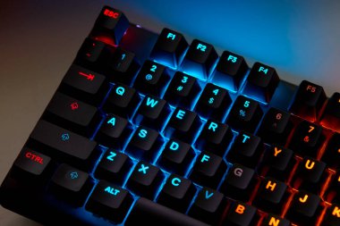 Renkli bir RGB mekanik oyun klavyesinin yakın çekimi canlı renklerle aydınlatılmış. Oyun ayarları için tasarlanmış modern bilgisayar aksesuarı, kişiselleştirilebilir arka ışıklandırma ve şık tasarım. 