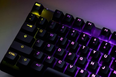 Renkli bir RGB mekanik oyun klavyesinin yakın çekimi canlı renklerle aydınlatılmış. Oyun ayarları için tasarlanmış modern bilgisayar aksesuarı, kişiselleştirilebilir arka ışıklandırma ve şık tasarım. 