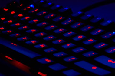 Renkli bir RGB mekanik oyun klavyesinin yakın çekimi canlı renklerle aydınlatılmış. Oyun ayarları için tasarlanmış modern bilgisayar aksesuarı, kişiselleştirilebilir arka ışıklandırma ve şık tasarım. 