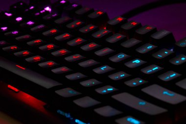 Renkli bir RGB mekanik oyun klavyesinin yakın çekimi canlı renklerle aydınlatılmış. Oyun ayarları için tasarlanmış modern bilgisayar aksesuarı, kişiselleştirilebilir arka ışıklandırma ve şık tasarım. 