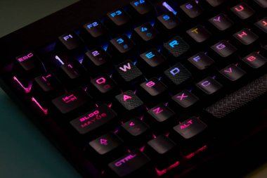 Renkli bir RGB mekanik oyun klavyesinin yakın çekimi canlı renklerle aydınlatılmış. Oyun ayarları için tasarlanmış modern bilgisayar aksesuarı, kişiselleştirilebilir arka ışıklandırma ve şık tasarım. 