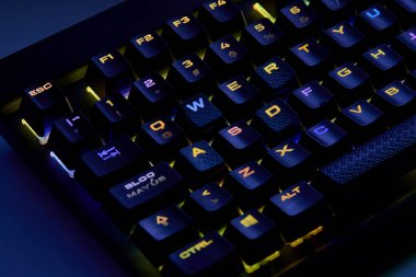 Renkli bir RGB mekanik oyun klavyesinin yakın çekimi canlı renklerle aydınlatılmış. Oyun ayarları için tasarlanmış modern bilgisayar aksesuarı, kişiselleştirilebilir arka ışıklandırma ve şık tasarım. 