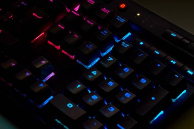 Renkli bir RGB mekanik oyun klavyesinin yakın çekimi canlı renklerle aydınlatılmış. Oyun ayarları için tasarlanmış modern bilgisayar aksesuarı, kişiselleştirilebilir arka ışıklandırma ve şık tasarım. 