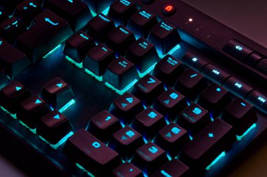 Renkli bir RGB mekanik oyun klavyesinin yakın çekimi canlı renklerle aydınlatılmış. Oyun ayarları için tasarlanmış modern bilgisayar aksesuarı, kişiselleştirilebilir arka ışıklandırma ve şık tasarım. 