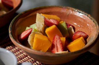 Sağlıklı ve renkli meyve karışımı taze kesilmiş muz, papaya ve çilek kabı örülmüş kil bir paspasın üzerinde servis edilir. Sürdürülebilir bir eko-locada yakalandı.