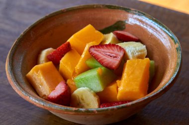 Sağlıklı ve renkli meyve karışımı taze kesilmiş muz, papaya ve çilek kabı örülmüş kil bir paspasın üzerinde servis edilir. Sürdürülebilir bir eko-locada yakalandı.
