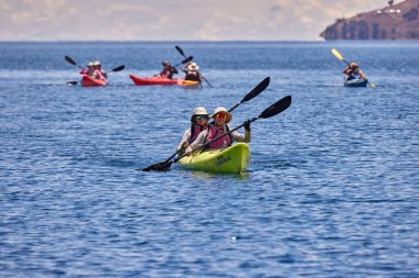 Bir grup deniz kayakçısı And Dağları 'nın engin, yüksek irtifa güzelliği ile çevrili Titicaca Gölü' nün derin mavi sularında huzur içinde süzülüyor. Puno Peru.