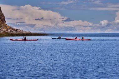 Bir grup deniz kayakçısı And Dağları 'nın engin, yüksek irtifa güzelliği ile çevrili Titicaca Gölü' nün derin mavi sularında huzur içinde süzülüyor. Puno Peru.