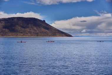 Bir grup deniz kayakçısı And Dağları 'nın engin, yüksek irtifa güzelliği ile çevrili Titicaca Gölü' nün derin mavi sularında huzur içinde süzülüyor. Puno Peru.