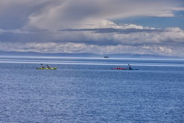 Bir grup deniz kayakçısı And Dağları 'nın engin, yüksek irtifa güzelliği ile çevrili Titicaca Gölü' nün derin mavi sularında huzur içinde süzülüyor. Puno Peru.