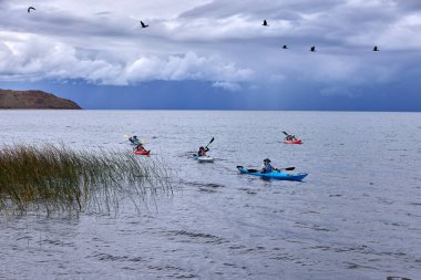 Bir grup deniz kayakçısı And Dağları 'nın engin, yüksek irtifa güzelliği ile çevrili Titicaca Gölü' nün derin mavi sularında huzur içinde süzülüyor. Puno Peru.