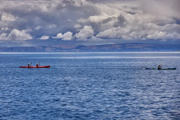 Bir grup deniz kayakçısı And Dağları 'nın engin, yüksek irtifa güzelliği ile çevrili Titicaca Gölü' nün derin mavi sularında huzur içinde süzülüyor. Puno Peru.