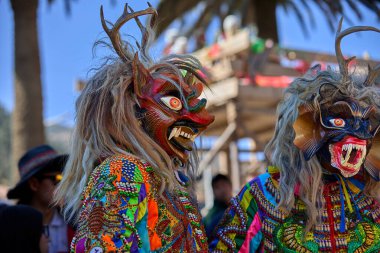 Şeytani maskeler ve akrobatik yeteneklerle, Saqras Paucartambo 'da dans ediyor, neşeli, alaycı ruhlar koruyor ve kışkırtıyor, enerji ve gerilim ekliyor. Bakire del Carmen