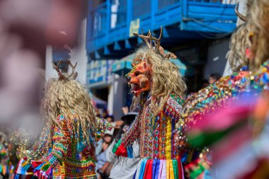 Şeytani maskeler ve akrobatik yeteneklerle, Saqras Paucartambo 'da dans ediyor, neşeli, alaycı ruhlar koruyor ve kışkırtıyor, enerji ve gerilim ekliyor. Bakire del Carmen