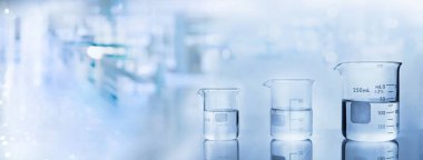 Kimya laboratuvarının arka planında su bulunan üç deney şişesi.