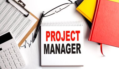 Not defterindeki PROJECT MANAGER metni beyaz arkaplanda pano ve hesap makinesi