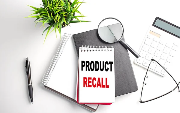 Text PRODUCT RECALL on a notebook with office tools on white background