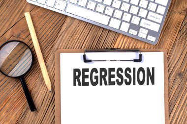 Tahta zemin üzerinde büyüteç ve klavye bulunan bir kağıt pano üzerindeki REGRESSION metni