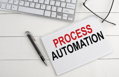Klavyeli bir not defterinde PROCESS AUTOMATION metni, beyaz ahşap arka planda kalem gözlüğü