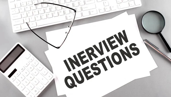 INTERVIEW QUESTIONS text on paper with keyboard, calculator on a grey background