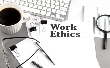 Gri arkaplanda büyüteç, kahve ve klavye ile kağıt üzerinde ETHICS metni çalış