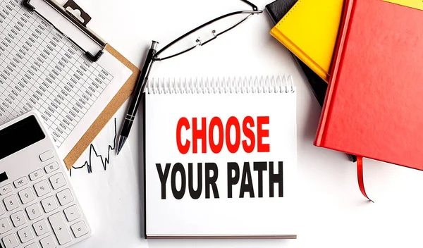 CHOOSE YOUR PATH text on notebook with clipboard and calculator on a white background