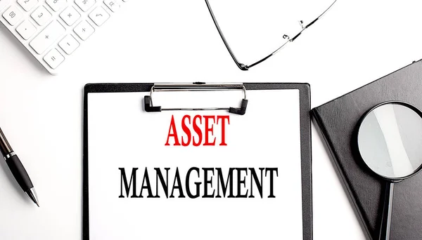 ASSET MANAGEMENT text written on a paper clipboard with office tools