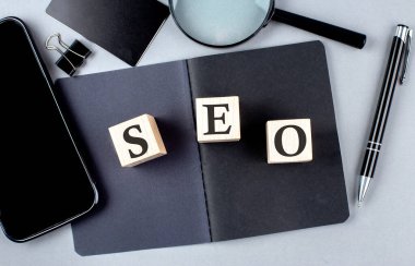 Word SEO, siyah bir defterde, akıllı pone, kredi kartı ve büyüteçle tahta blokta.