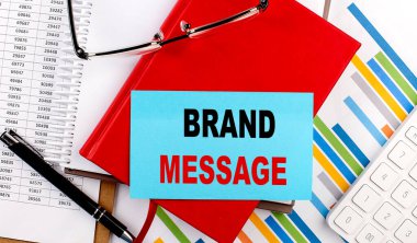 Çizelge arkaplanındaki kırmızı defter üzerindeki bir yapışkan üzerinde Brand MESAGE metni