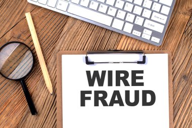 Kağıt pano üzerine WIRE FRAUD metin ahşap bir zemin üzerinde büyüteç ve klavye ile