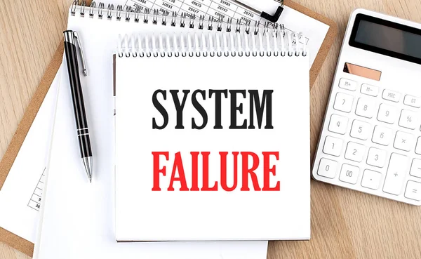 SYSTEM FAILURE is written in white notepad near a calculator, clipboard and pen. Business