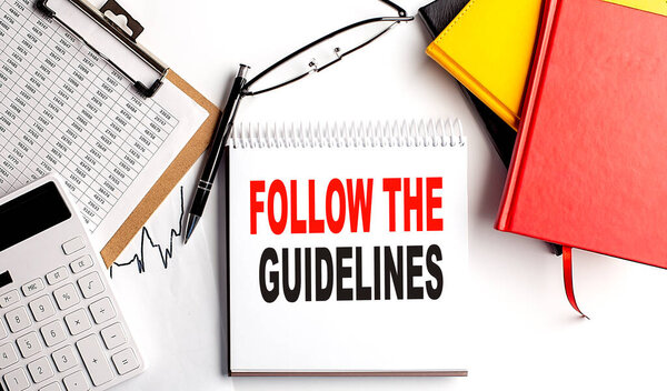 FOLLOW THE GUIDELINES text on notebook with clipboard and calculator on a white background