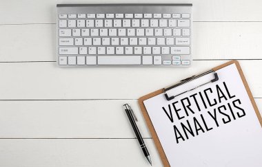 Beyaz ahşap bir arka plan, iş konsepti üzerine VERTICAL ANALYSIS yazılı klavye, pano ve kalem ile ev ofis çalışma alanı