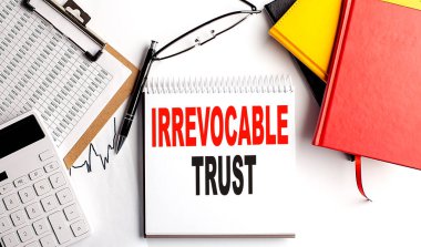 IRREVOCABLE TRUST text on notebook with clipboard and calculator on a white background clipart