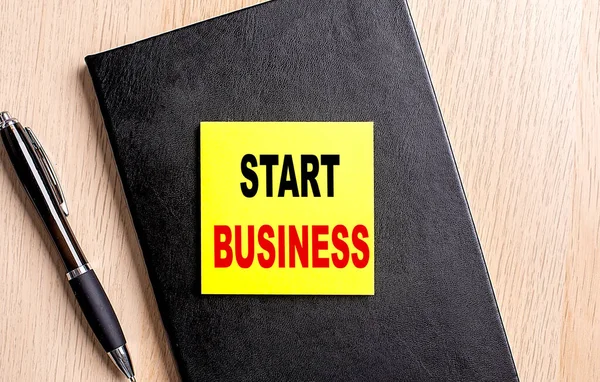 START BUSINESS text on sticky on black notebook with pen