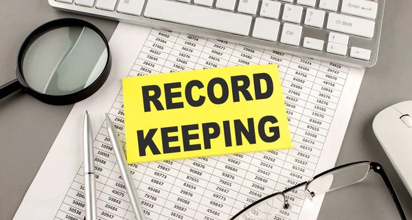 RECORD KEEPING text written on sticky on chart with keyboard and magnifier