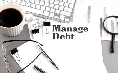 MANAGE DEBT text on a paper with magnifier, coffee and keyboard on a grey background clipart