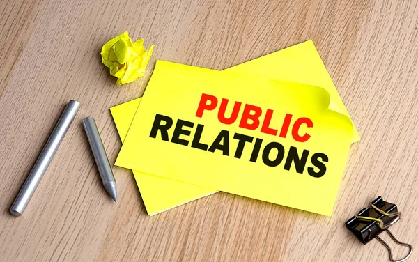 PUBLIC RELATIONS text on a yellow sticky on wooden background