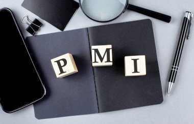 Word PMI on a wooden block on black notebook with smartpone, credit card and magnifier