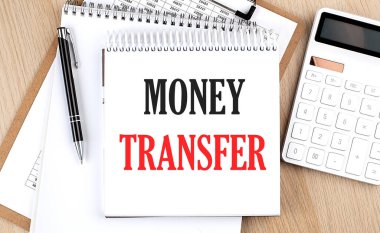 MONEY TRANSFER is written in white notepad near a calculator, clipboard and pen. Business