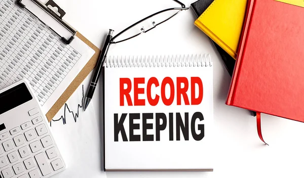 RECORD KEEPING text on notebook with clipboard and calculator on a white background