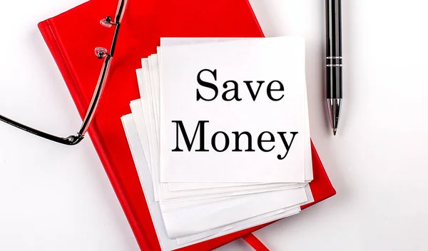 SAVE MONEY text on a sticker on red notebook with pen and glasses
