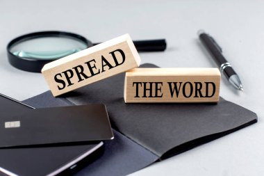 SPREAD THE WORD text on a wooden block on black notebook , business concept clipart