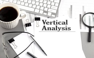 VERTICAL ANALYSIS text on a paper with magnifier, coffee and keyboard on a grey background