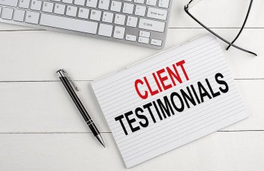 CLIENT TESTIMONIALS text on notebook with keyboard , pen glasses on a white wooden background